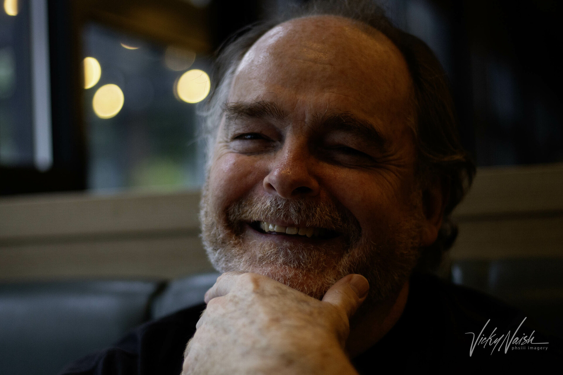 a portrait of a smilining bearded man with his hand on his chin